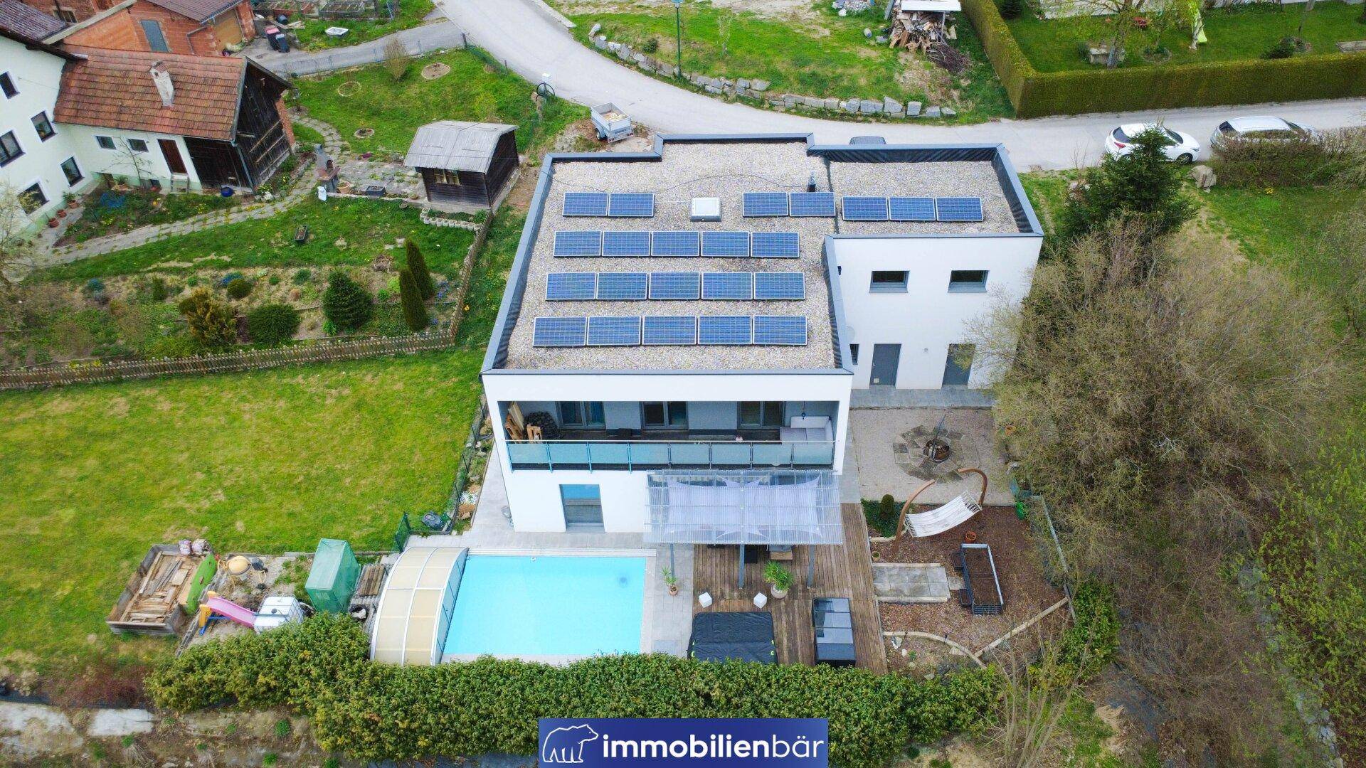 Luftaufnahme des modernen Hauses mit Flachdach, Solaranlage und großem Gartenbereich.