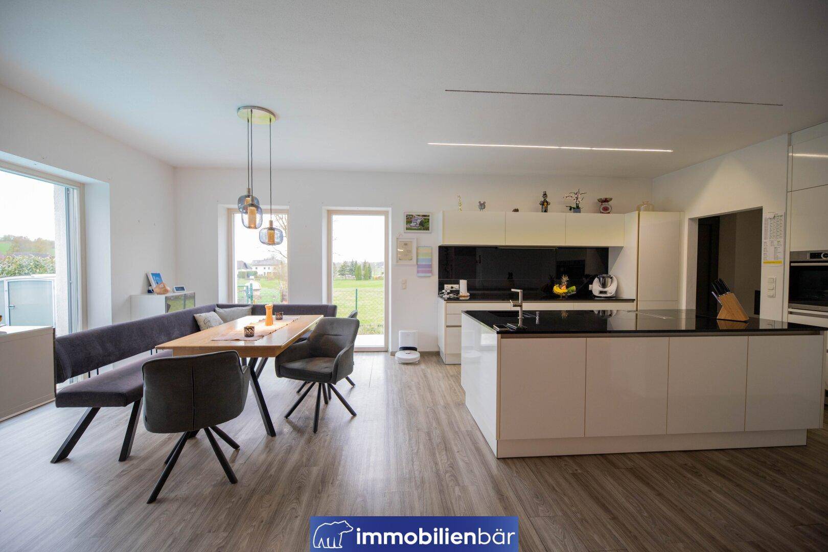 Helle, moderne Küche mit Kochinsel und Essbereich, ausgestattet mit hochwertigen Geräten und viel Licht.