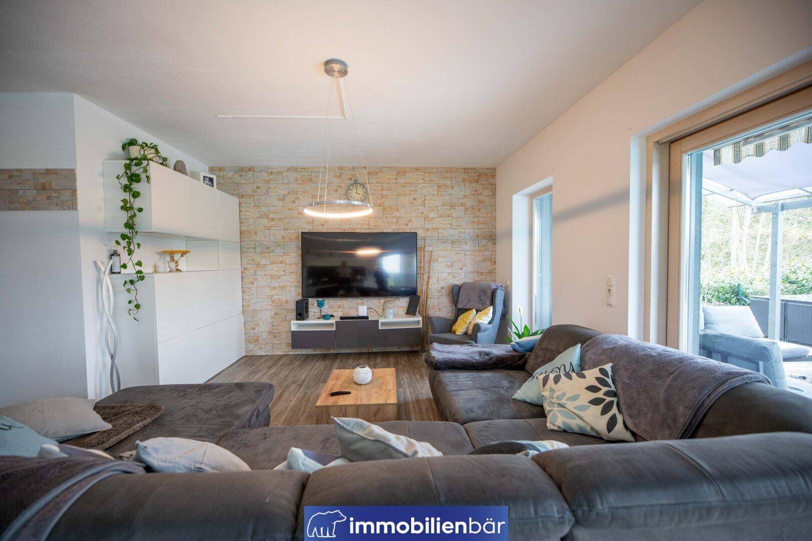 Gemütliches Wohnzimmer mit großem Ecksofa und Steinwandakzent, mit Zugang zur Terrasse.