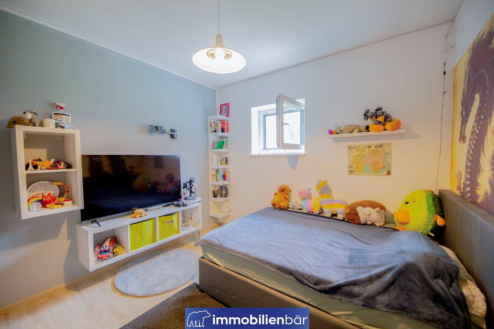 Kinderzimmer mit Bett, Fernseher und Fenster, das viel Tageslicht hereinlässt.
