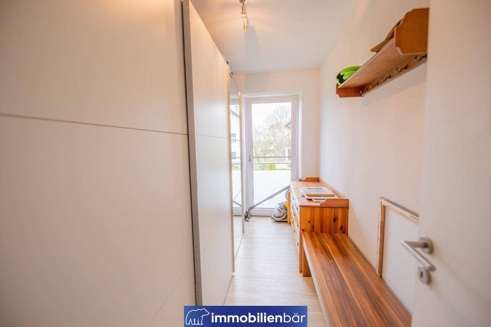 Heller Flur mit Einbauschränken und einer Holzbank, die zum Balkon führt.