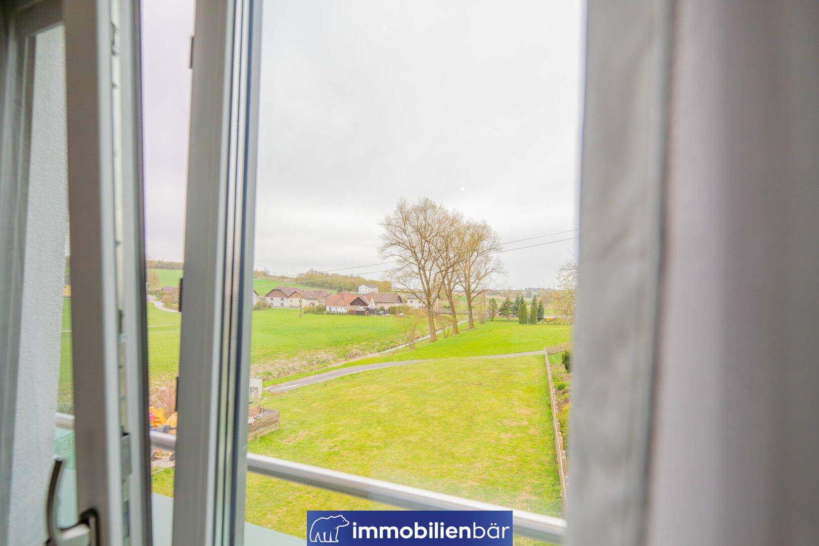 Weitläufiger Blick auf die grüne Landschaft und umliegende Häuser aus dem Fenster.