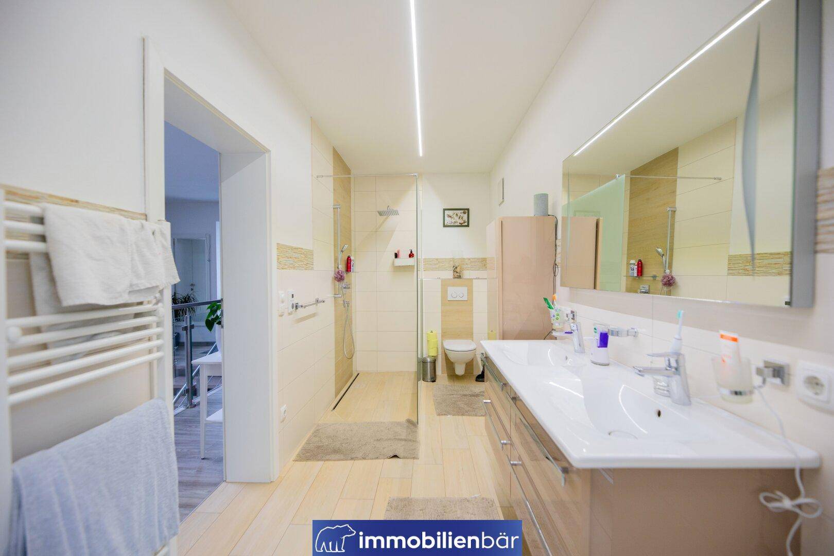 Geräumiges Badezimmer mit Doppelwaschbecken, begehbarer Dusche und WC.