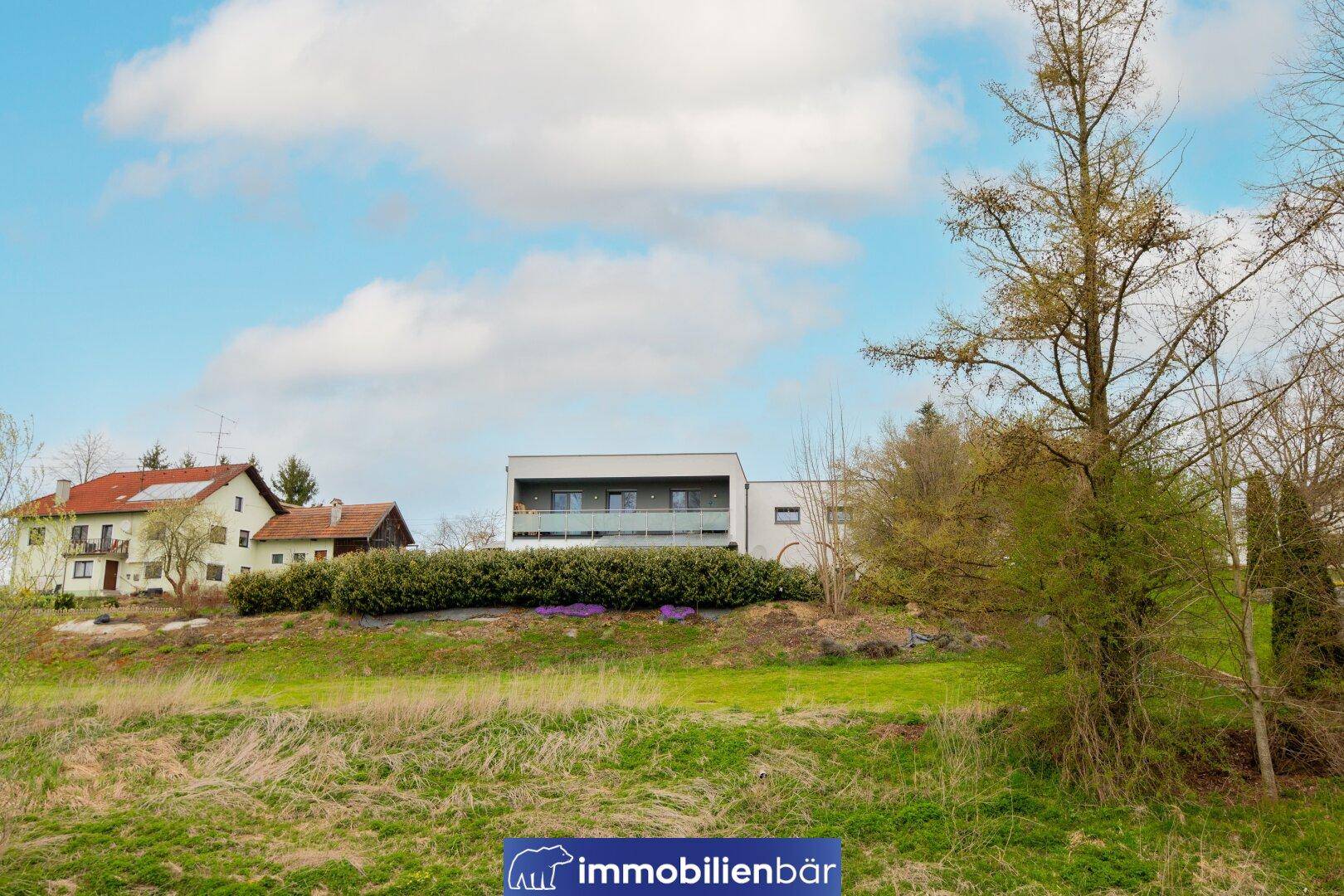 Modernes Wohnhaus in ländlicher Umgebung, eingebettet in grüne Hügel und Bäume.
