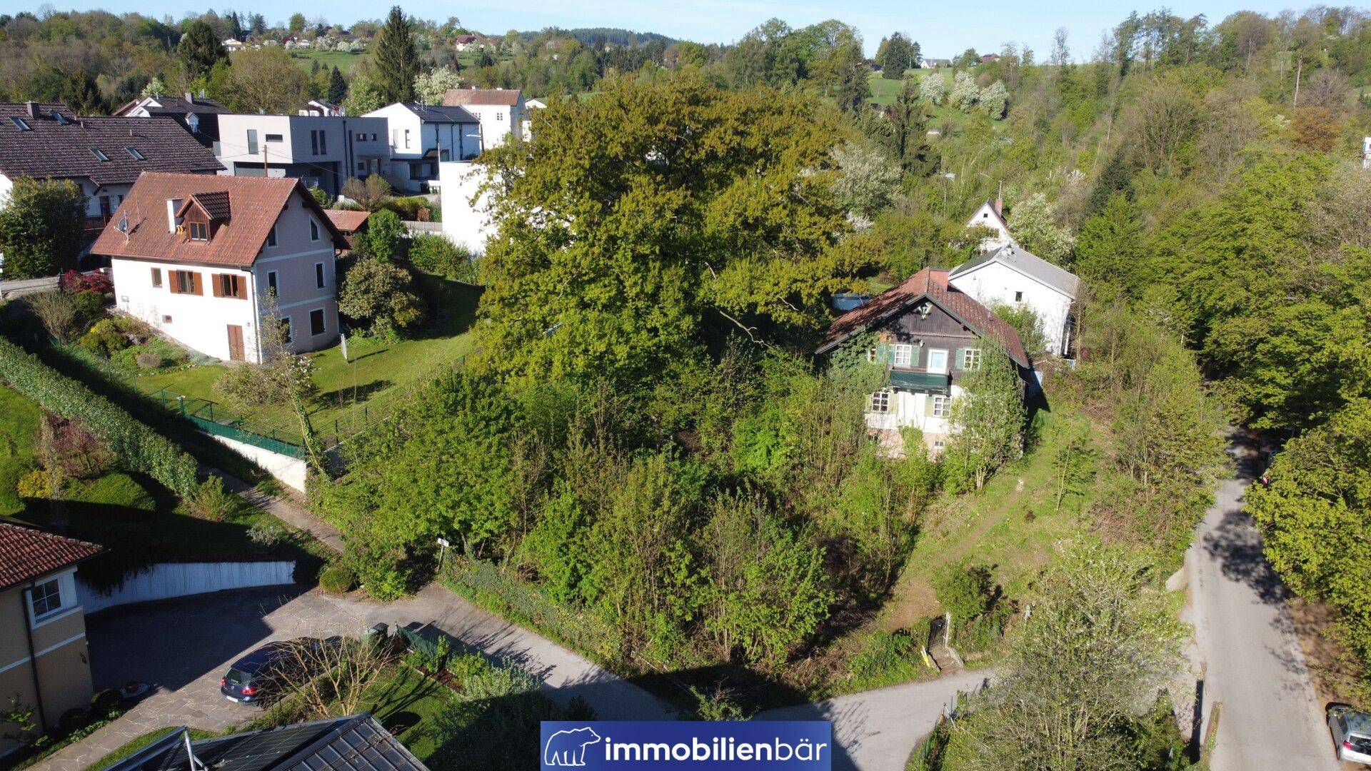 Luftaufnahme einer Wohnsiedlung mit verschiedenen Häusern und üppiger Vegetation in Hanglage.