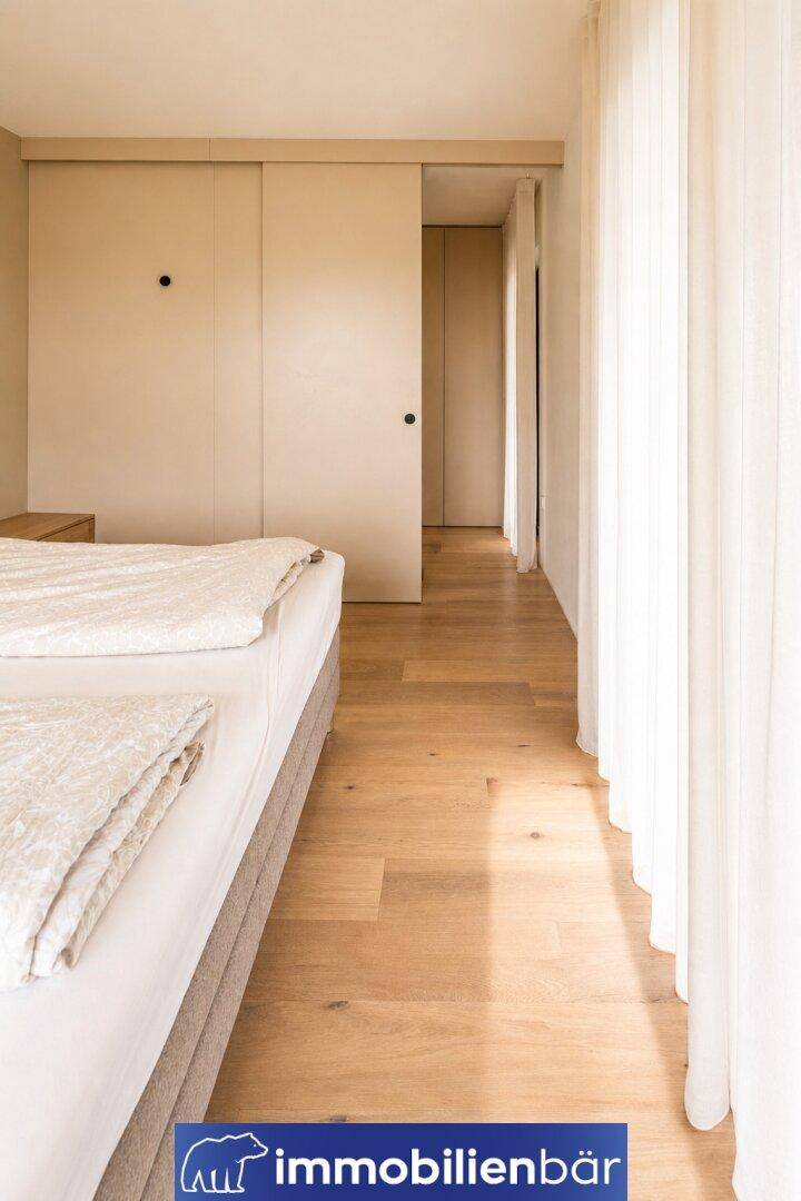 Helles Schlafzimmer mit Holzboden, beigem Bett und integrierten Schiebetüren.