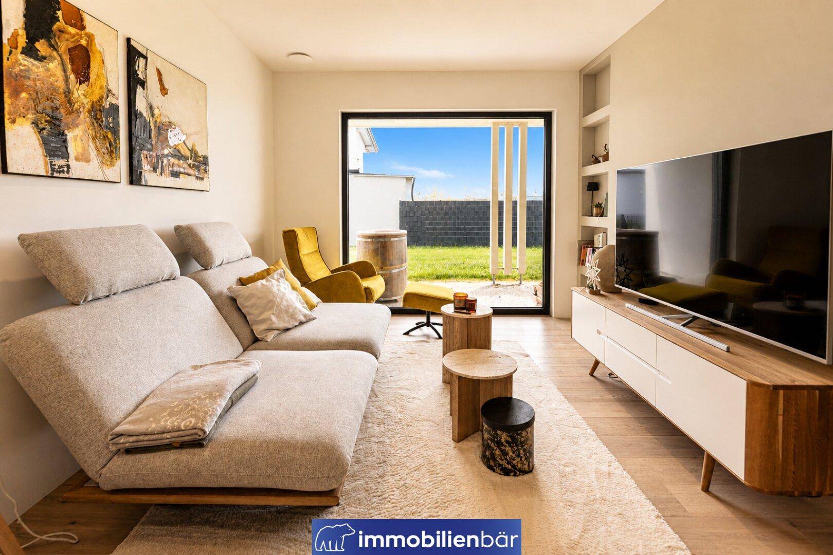 Gemütliches Wohnzimmer mit Sofa, Fernseher und großem Zugang zum Gartenbereich.