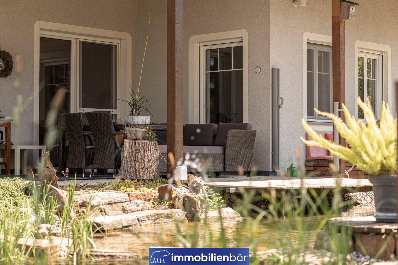 Entspannungsbereich auf der überdachten Terrasse mit Blick auf den Teich und die Gartenlandschaft.
