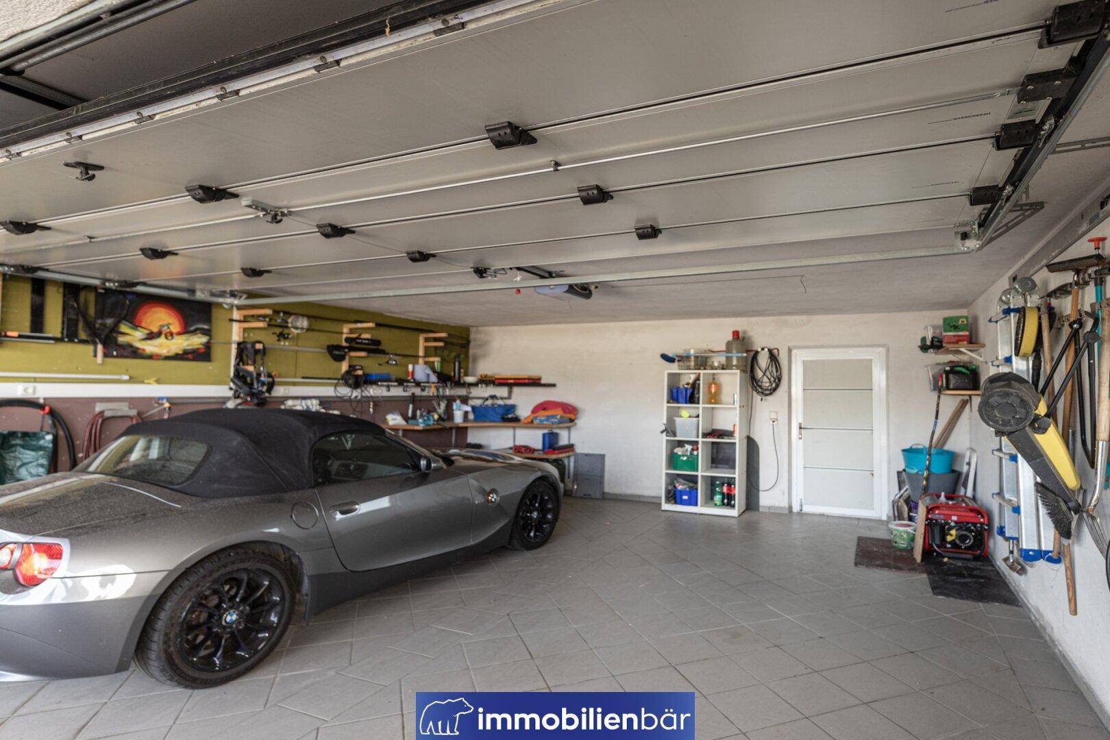 Geräumige Garage mit Platz für ein Auto und verschiedenen Werkzeugen an den Wänden.