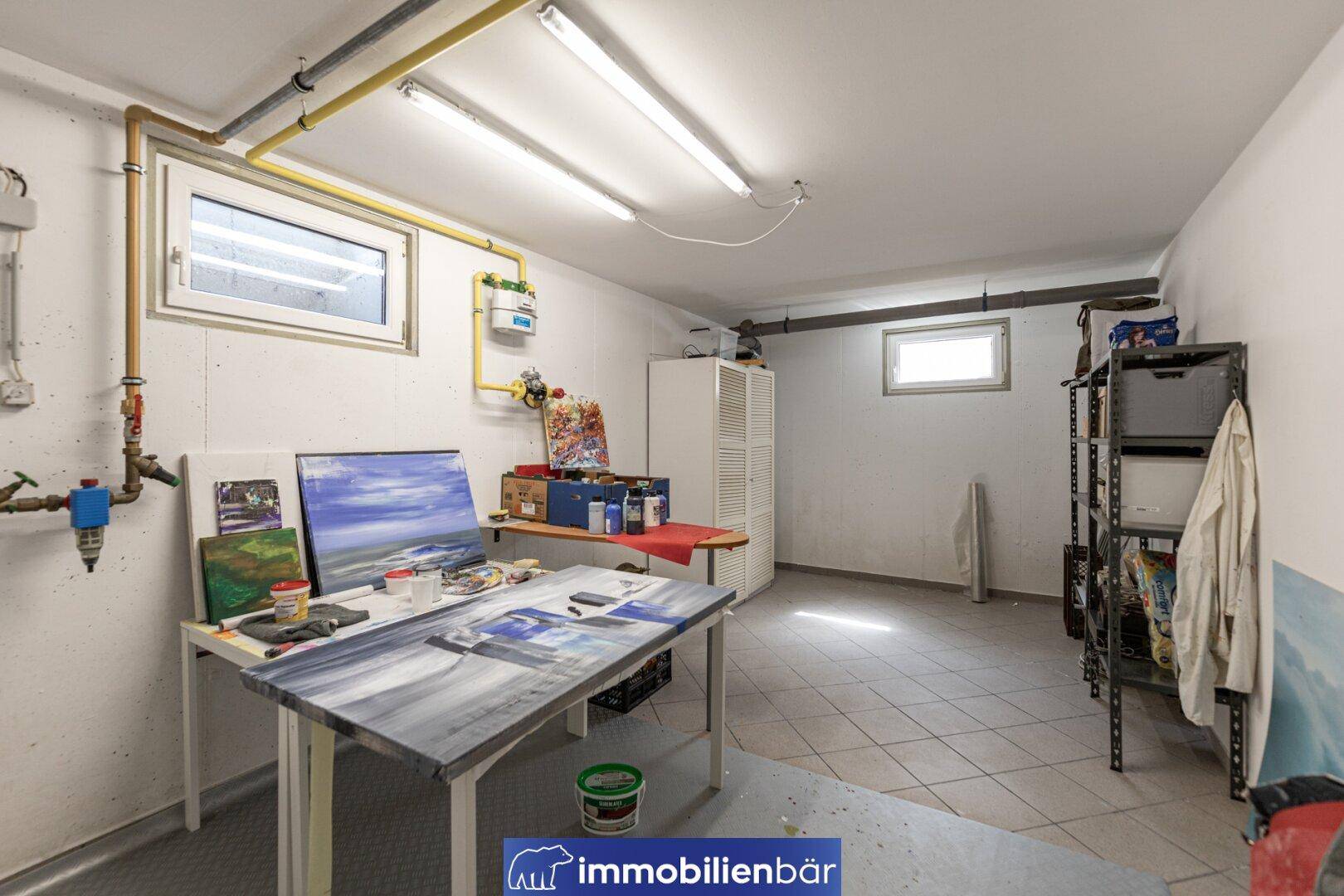 Heller Hobbyraum im Keller mit Fenstern, Werkbank und Fliesenboden.