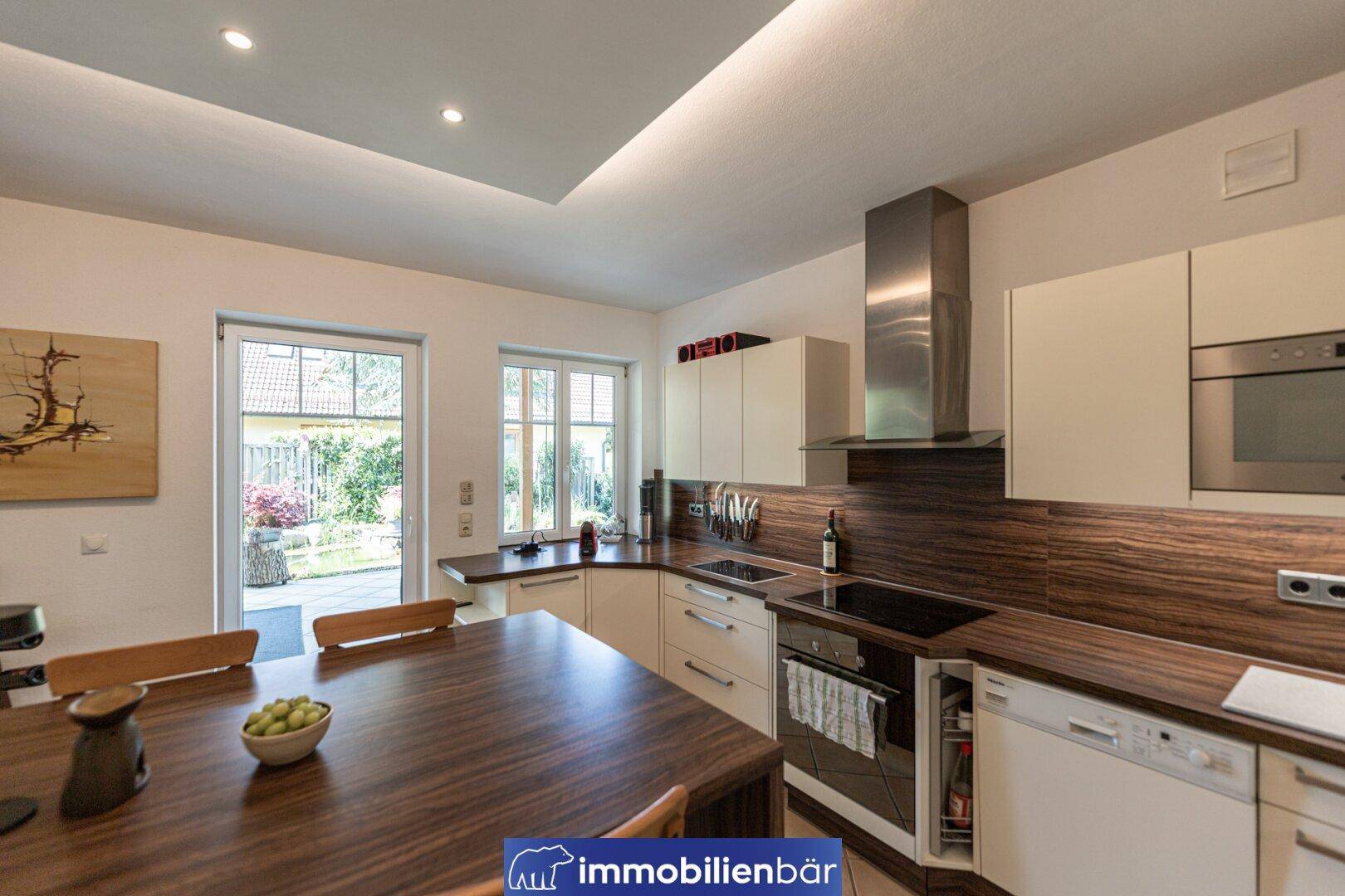 Moderne Küche mit Holzarbeitsplatten, integrierten Geräten und Essbereich mit Gartenzugang.