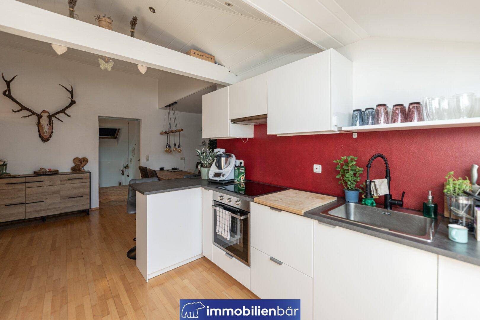 Moderne Küche mit weißen Fronten, roter Wand und Blick auf den offenen Wohnbereich.