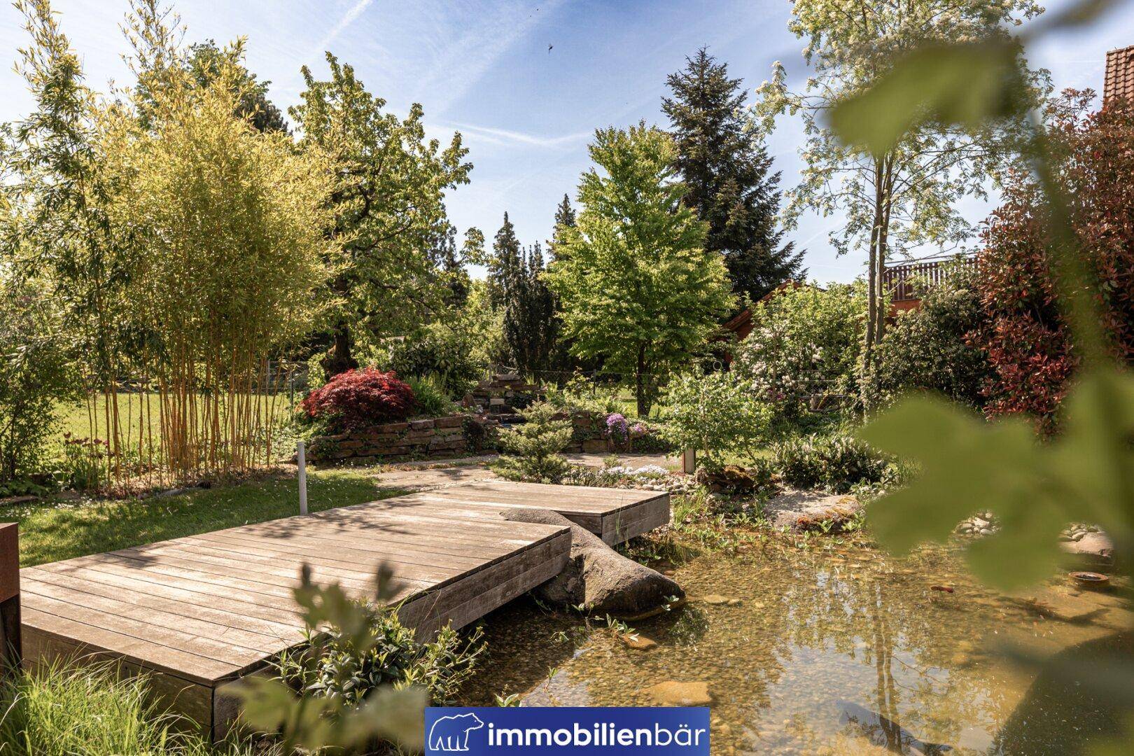 Malerischer Gartenbereich mit Teich, Holzsteg und üppiger, vielfältiger Bepflanzung.