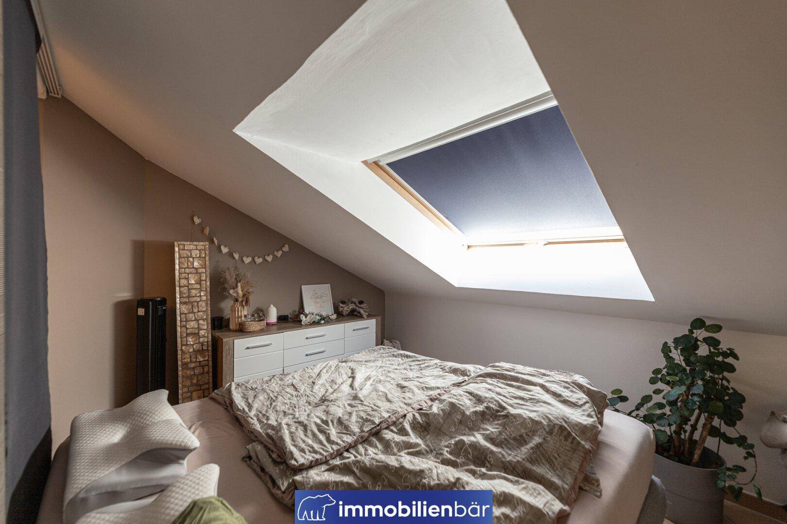 Schlafzimmer im Dachgeschoss mit schrägen Wänden, Dachfenster und hellem Holzboden.
