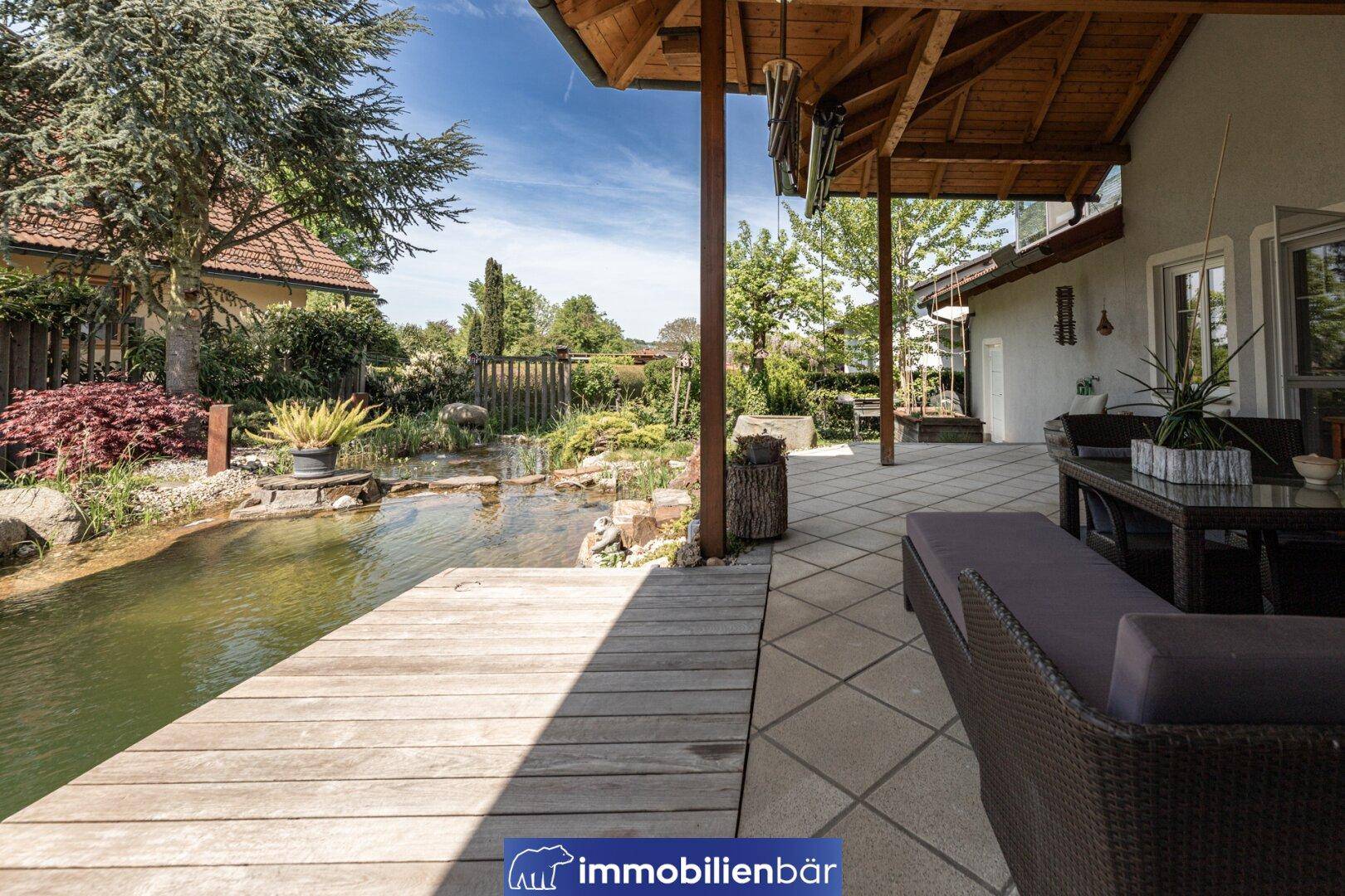 Gemütliche überdachte Terrasse mit Rattanmöbeln und direktem Zugang zum Gartenteich.