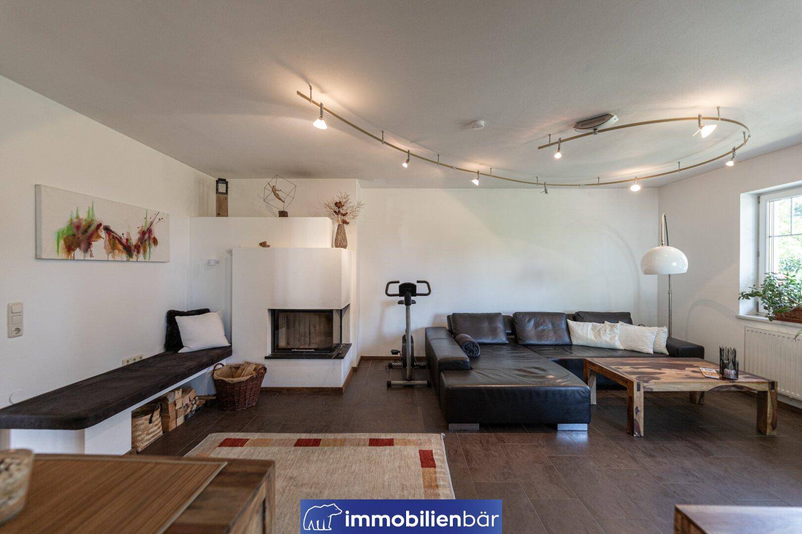 Gemütliches Wohnzimmer mit Kamin, dunklem Ledersofa und modernem Beleuchtungskonzept.