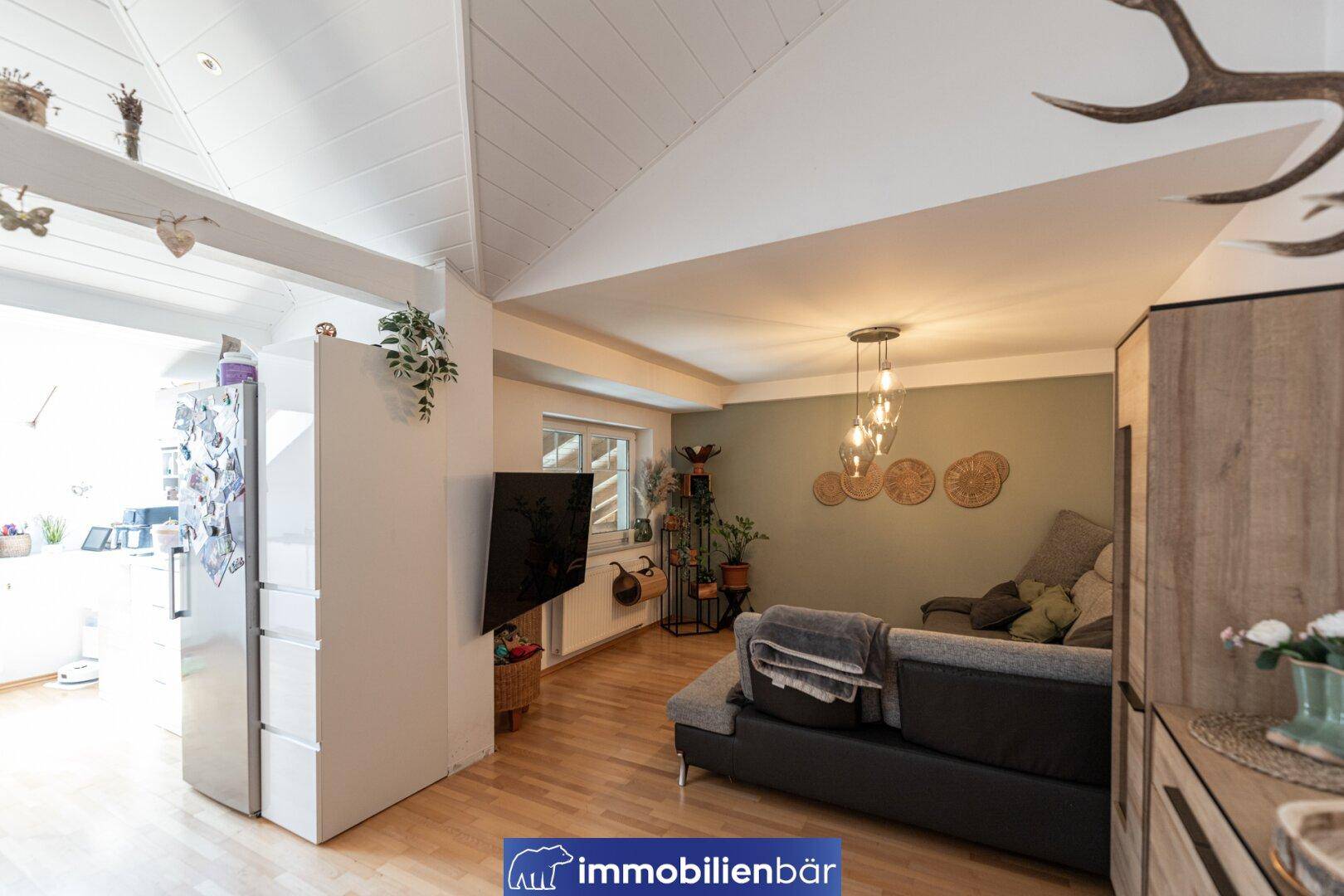 Offener Wohnbereich mit Sofa, Fernseher und Blick in die angrenzende Küche.