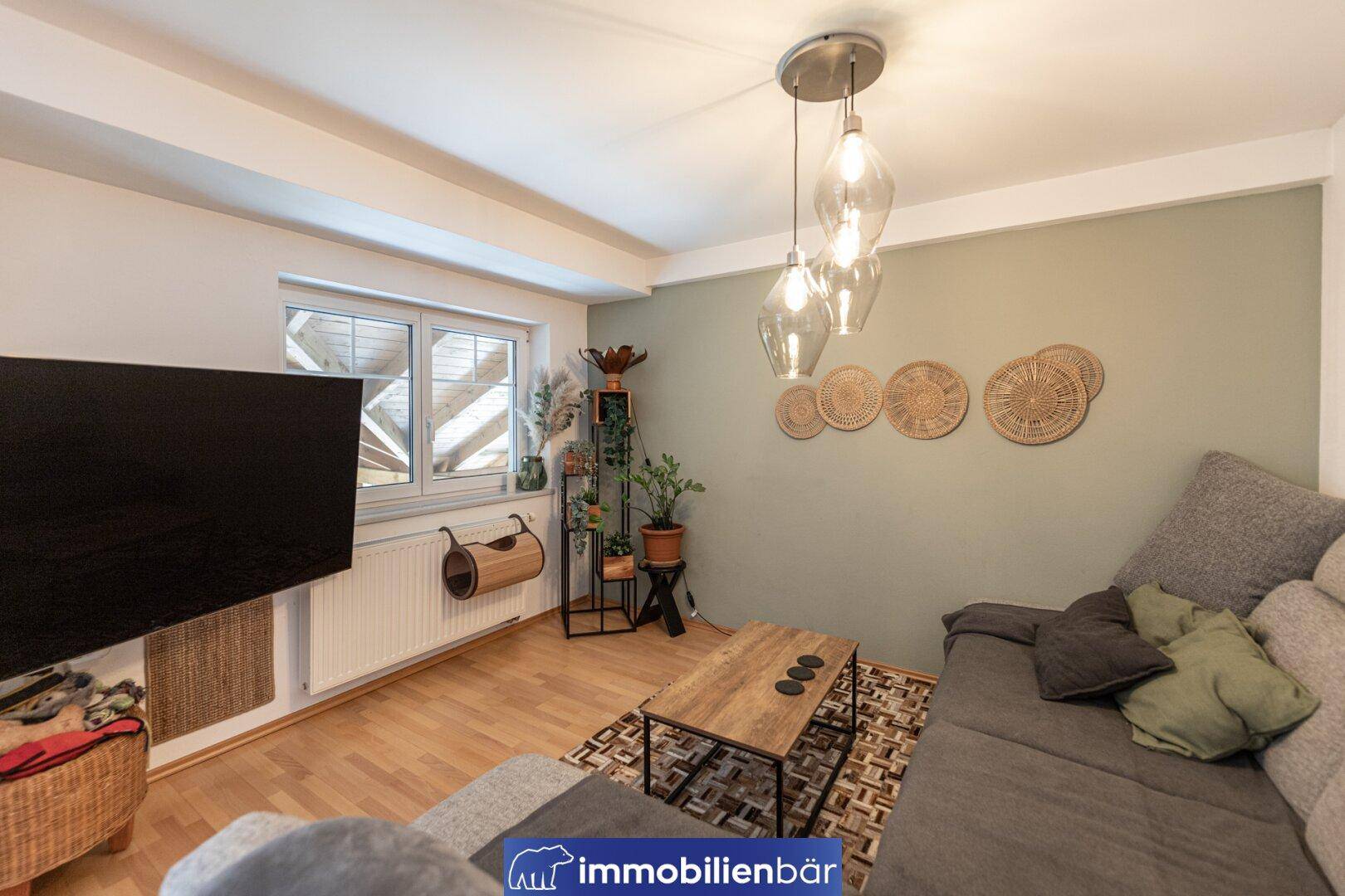 Gemütliches Wohnzimmer mit Sofa, Holzboden und einer Wand in sanftem Grünton.