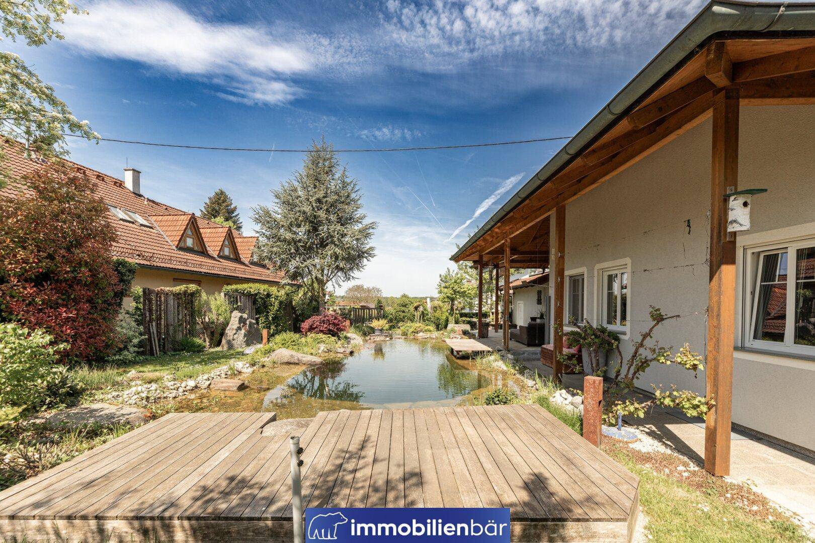 Großzügige überdachte Terrasse mit Holzdeck, das sich über den idyllischen Gartenteich erstreckt.