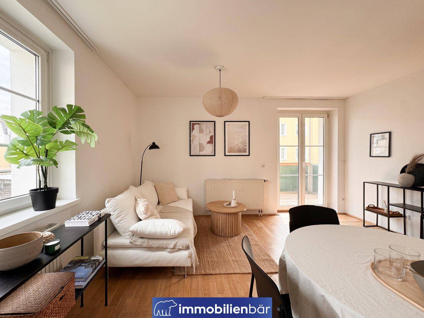 Lichtdurchfluteter Wohnbereich mit Holzboden, bequemer Couch und Zugang zum Außenbereich.