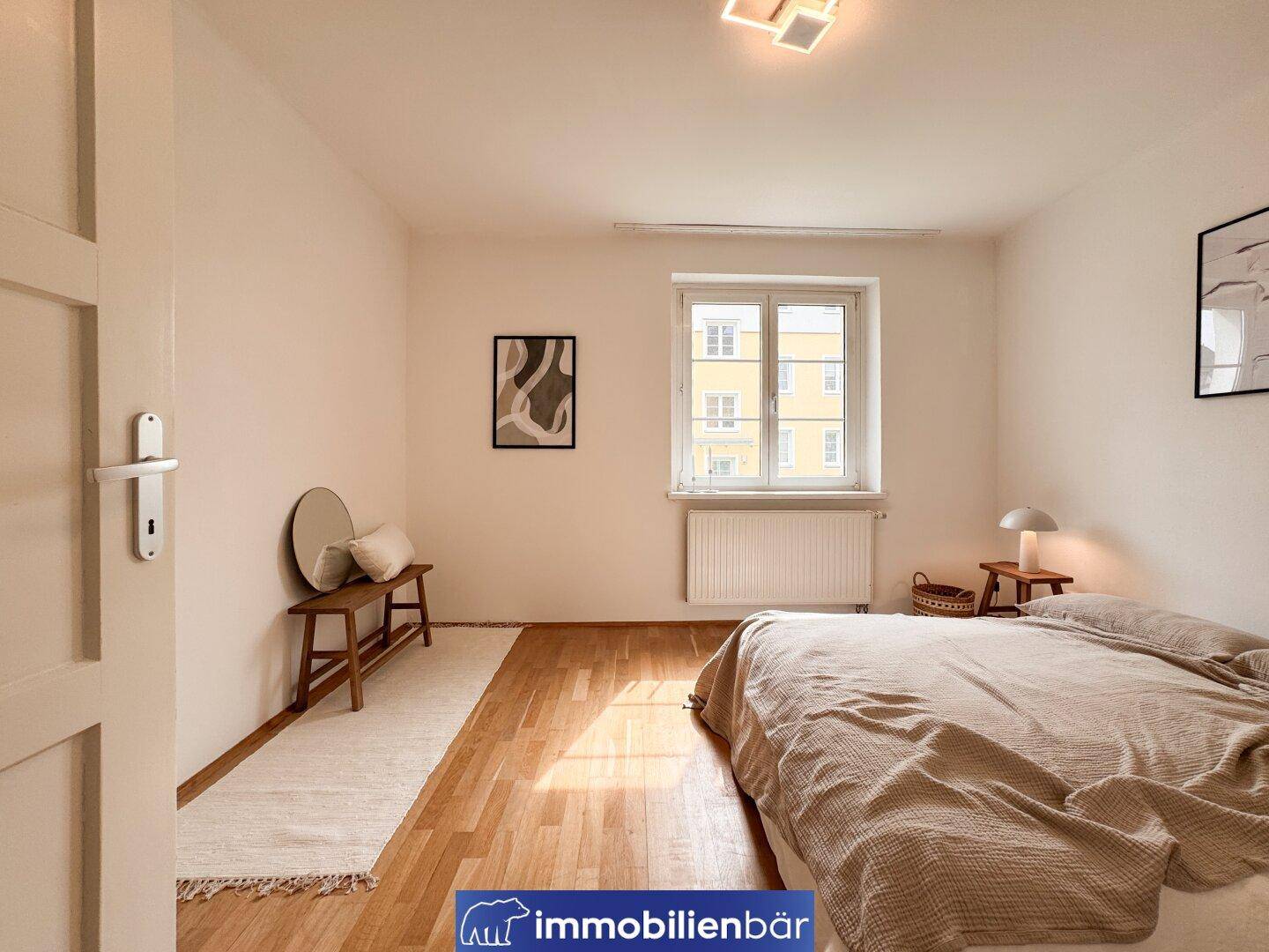 Gemütliches Schlafzimmer mit Holzboden, großem Fenster und viel natürlichem Licht.
