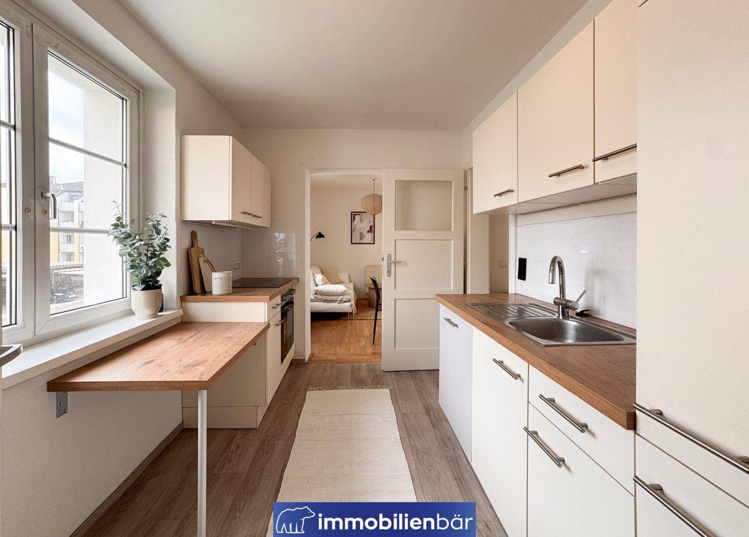 Funktionale Küche mit weißen Schränken, Holzarbeitsplatten und Fenster mit Ausblick.