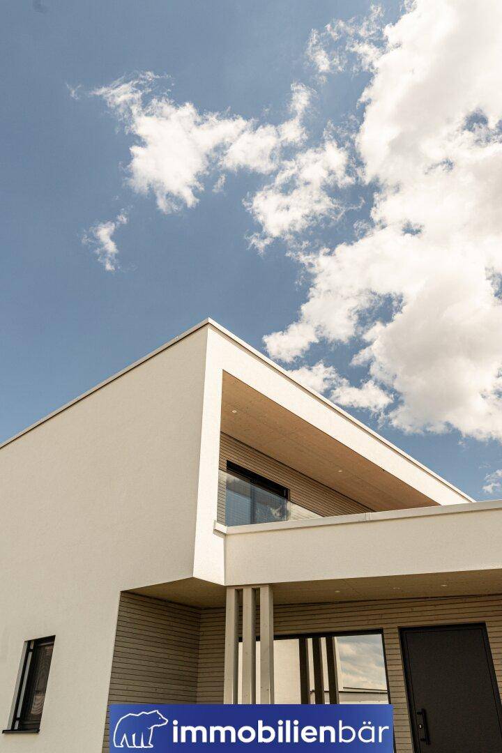 Architektonisches Detail der modernen Fassade mit Holzelementen und Glasgeländer unter blauem Himmel.
