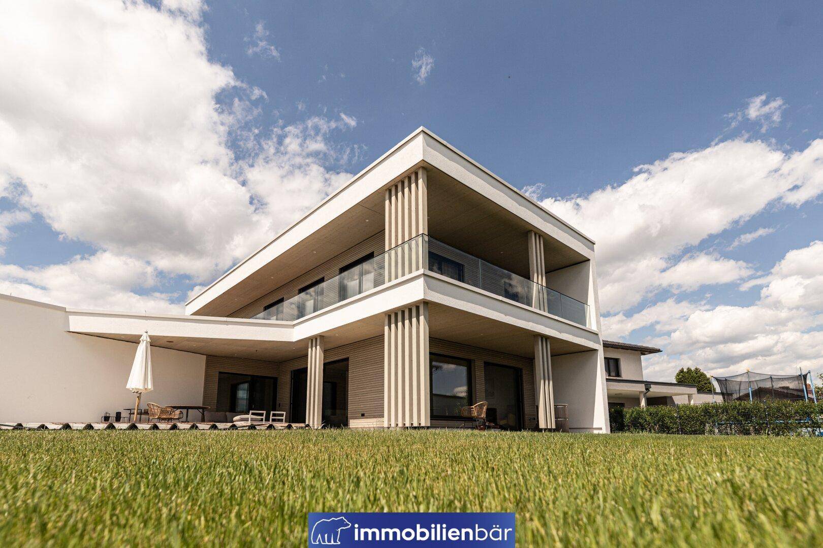 Moderne Villa von hinten mit großzügigen Terrassen und einem weitläufigen grünen Garten.