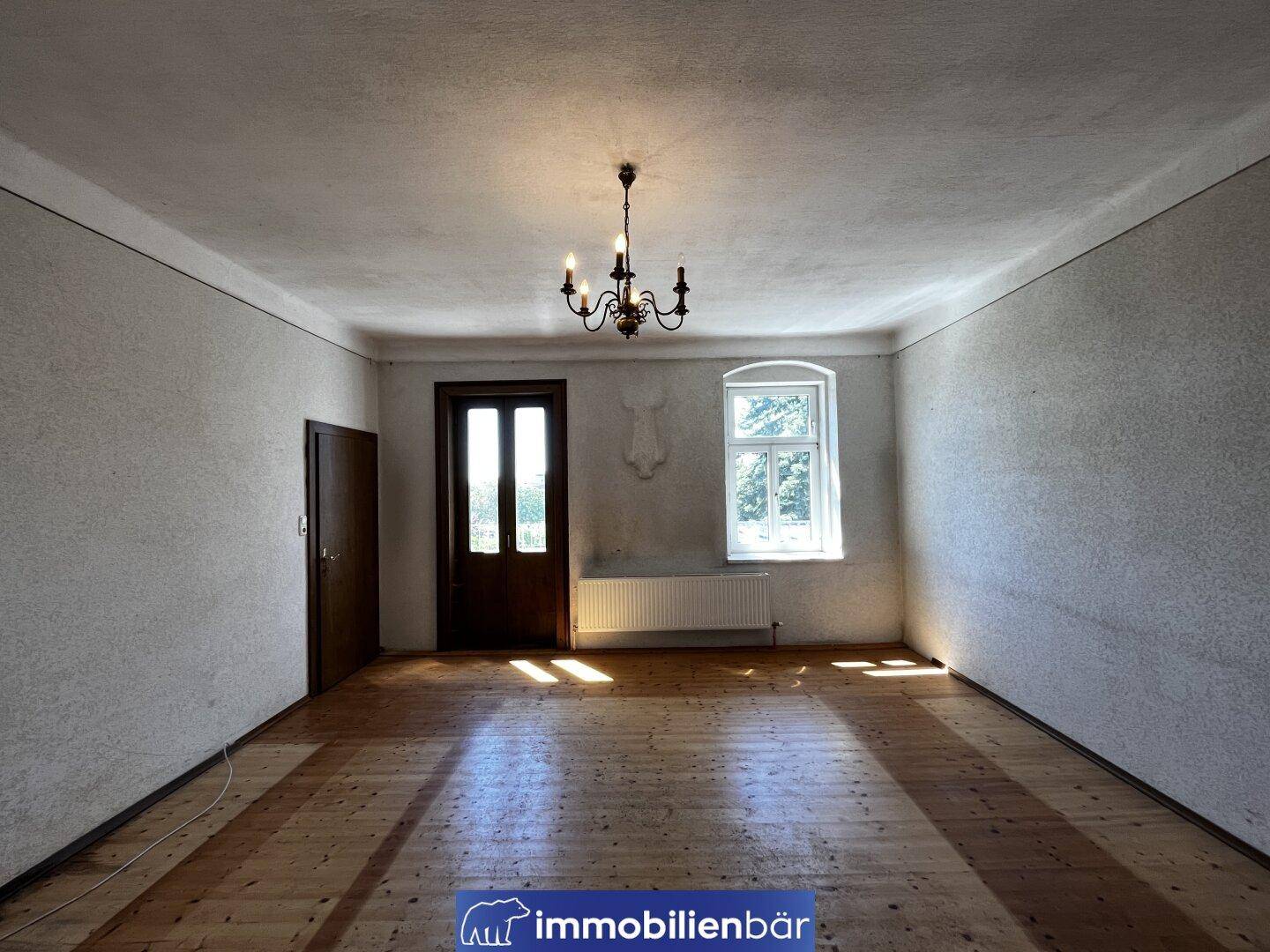 Geräumiges, unmöbliertes Zimmer mit Holzdielenboden, hohen Decken und einem Fenster.