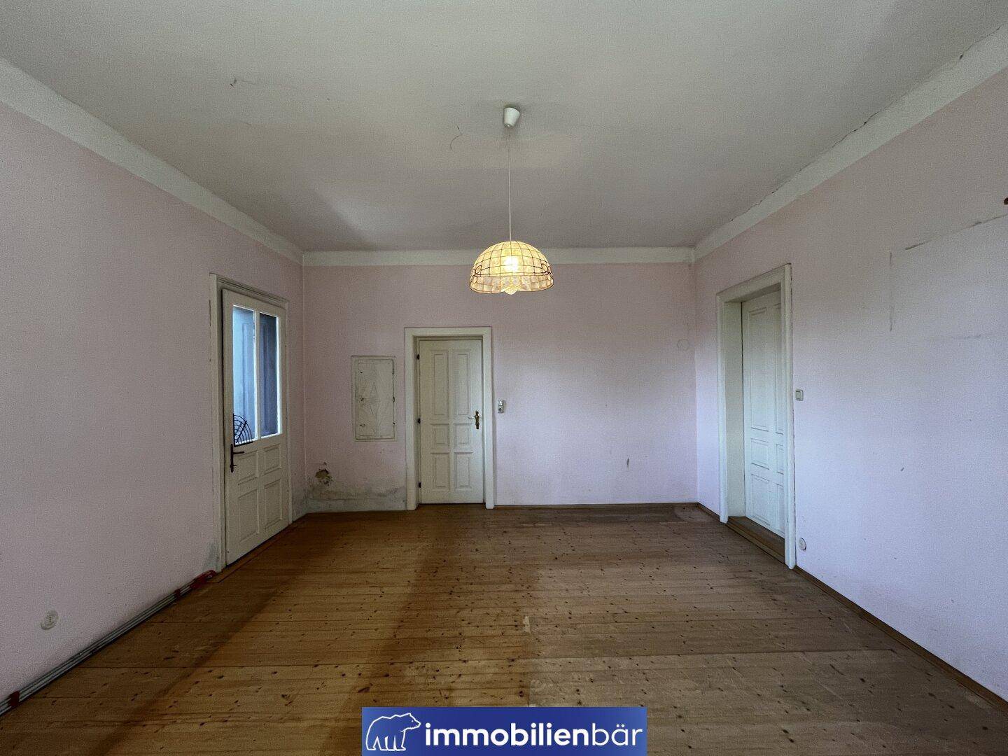 Helles, unmöbliertes Zimmer mit Holzdielenboden und rosa gestrichenen Wänden.