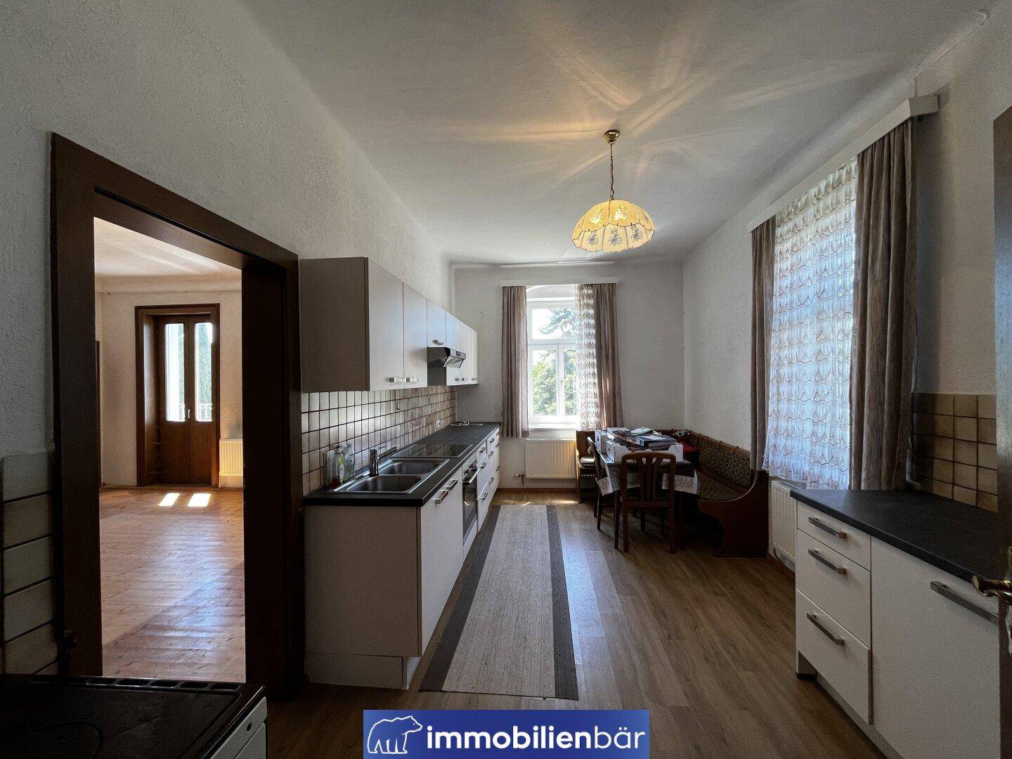 Einfache Küche mit weißen Schränken, Fliesenrückwand und Essbereich am Fenster.