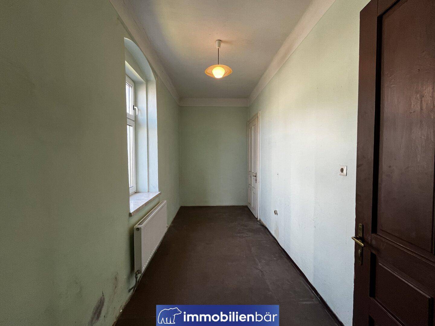 Schmaler Flur mit grünen Wänden, dunklem Boden und einem Fenster.