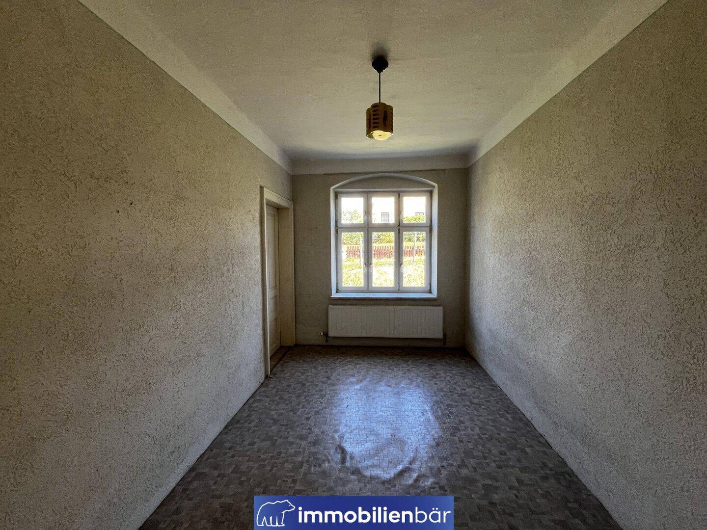 Leeres Zimmer mit Linoleumboden, beigen Wänden und einem Fenster mit Blick nach draußen.
