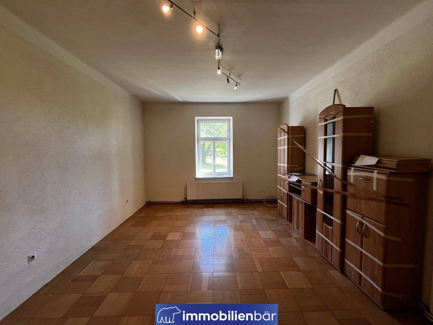 Geräumiges Zimmer mit Parkettboden, einem Fenster und Holzschränken.