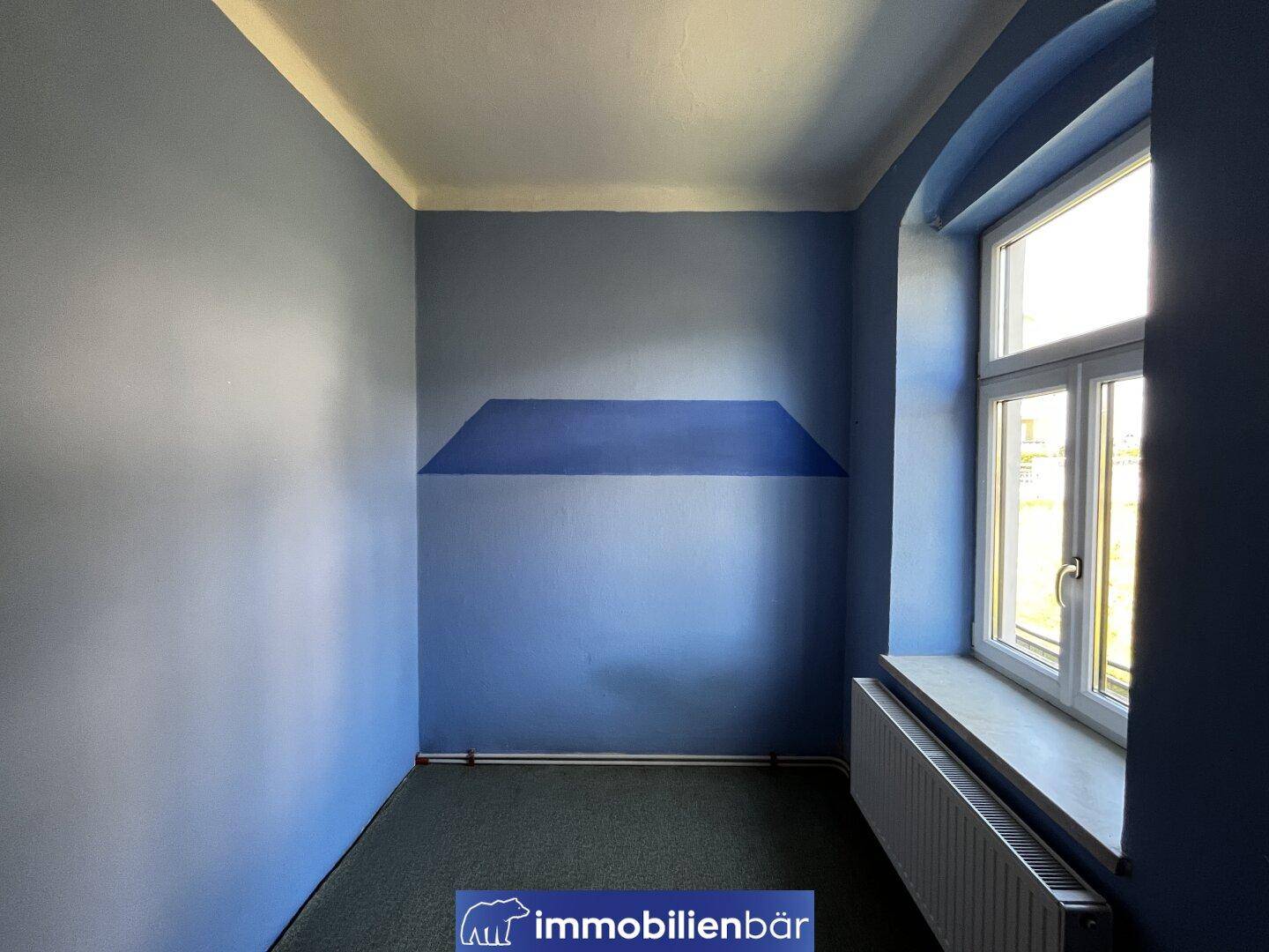 Kleines Zimmer mit blauen Wänden, Teppichboden und einem Fenster.