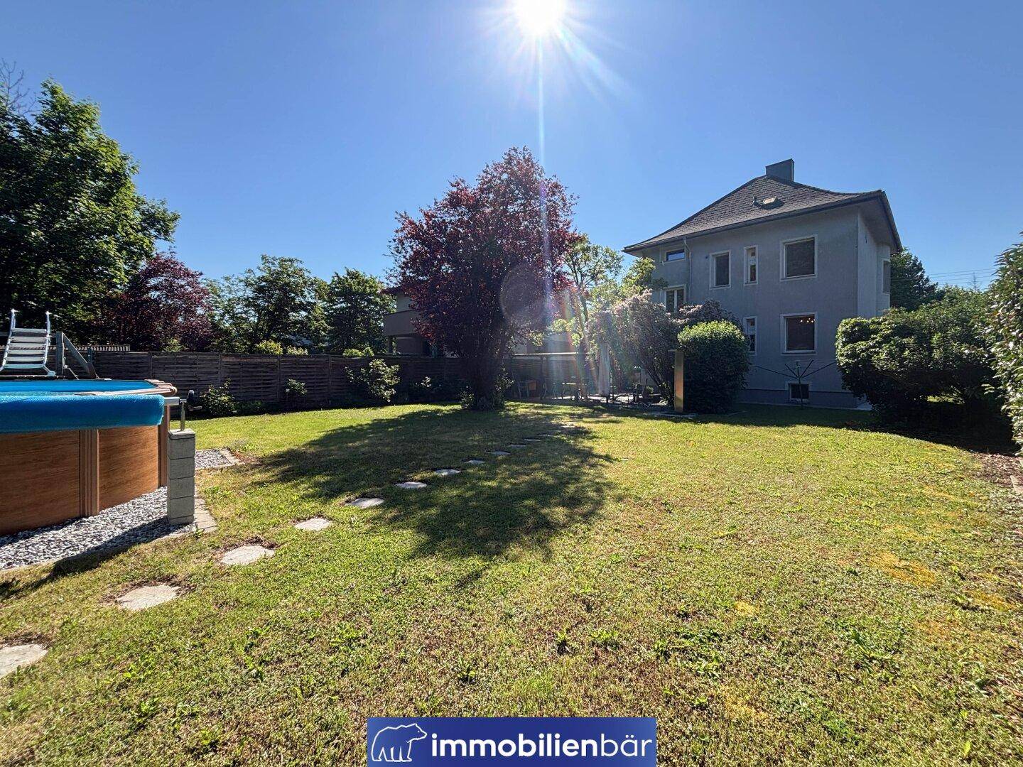 Großer, sonniger Garten mit Rasenfläche, Aufstellpool und dem Haus im Hintergrund.