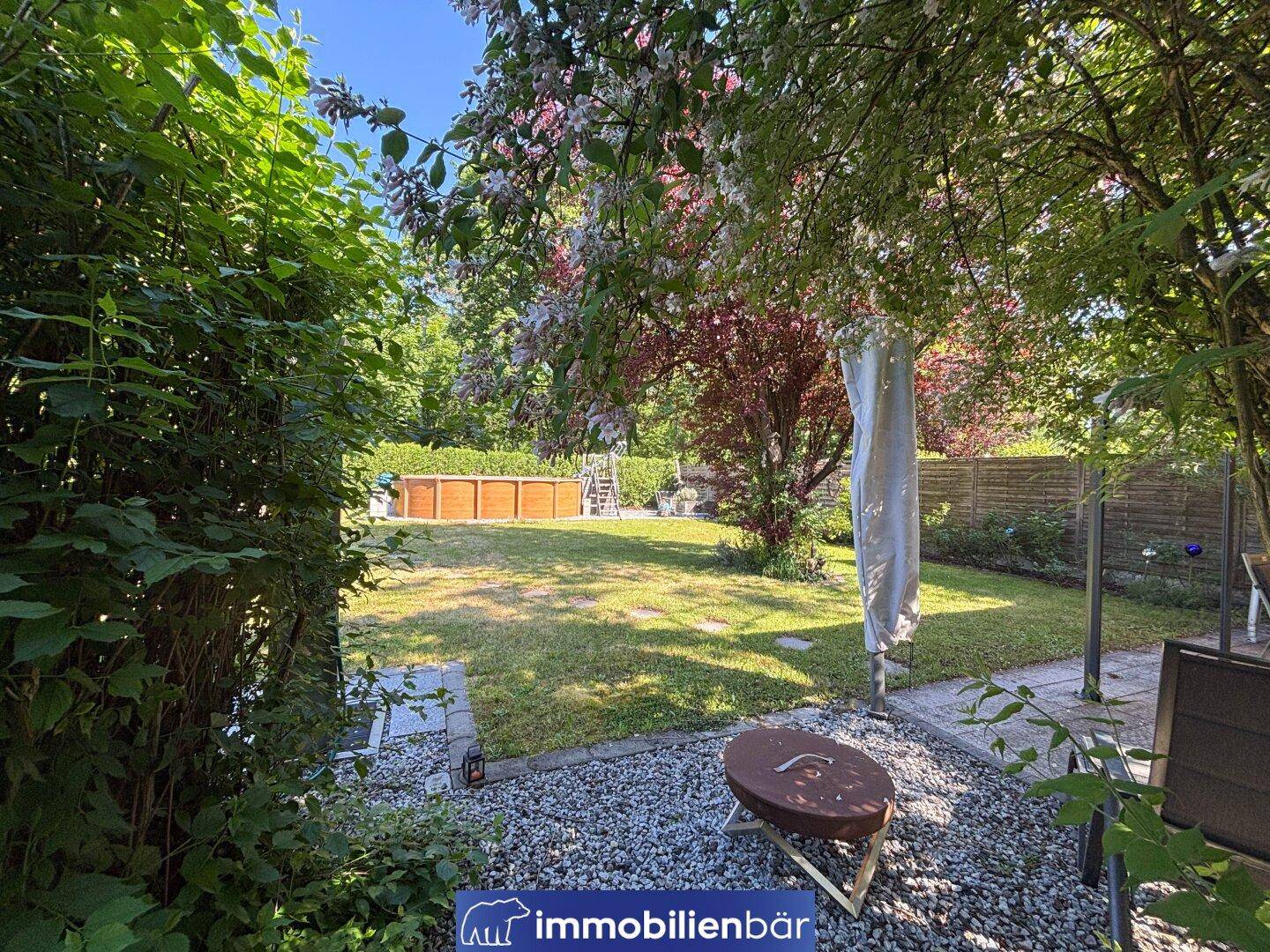 Blick in den grünen Garten mit Rasenfläche, Bäumen und einem Aufstellpool im Hintergrund.