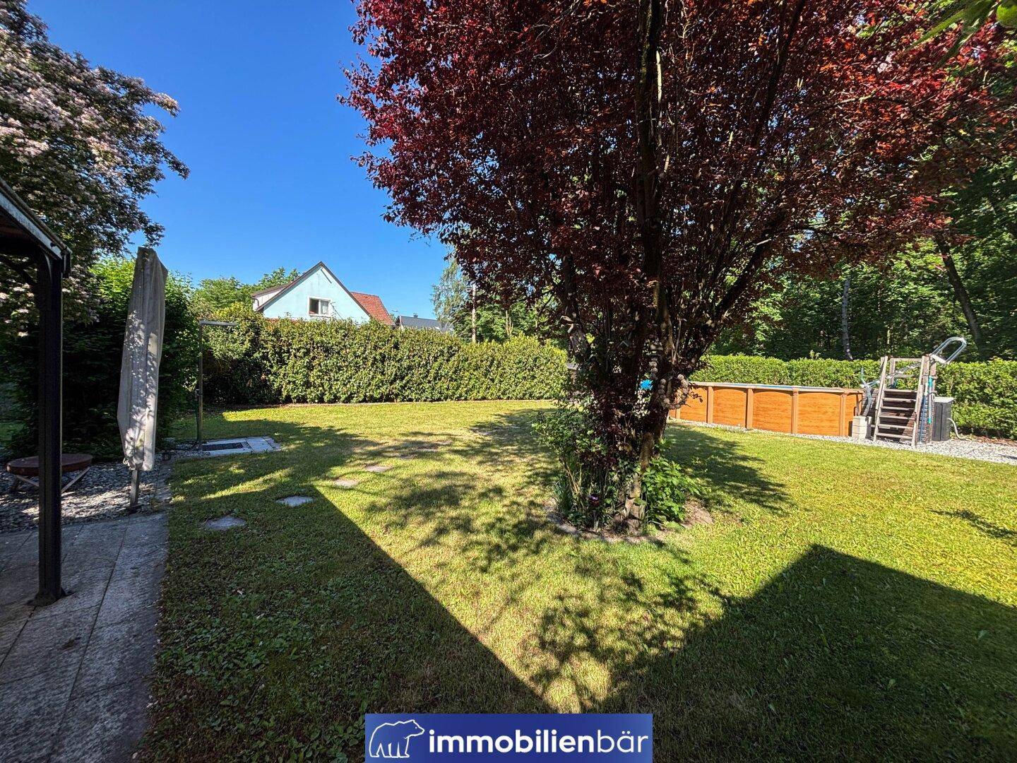 Weitläufige Rasenfläche im Garten mit einem Baum und einem Aufstellpool im hinteren Bereich.