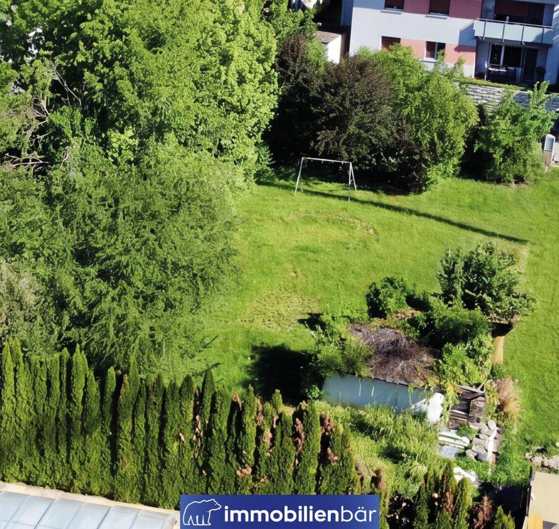 Luftaufnahme des weitläufigen Gartens mit Rasenfläche, Hecke und einem kleinen Schuppen.