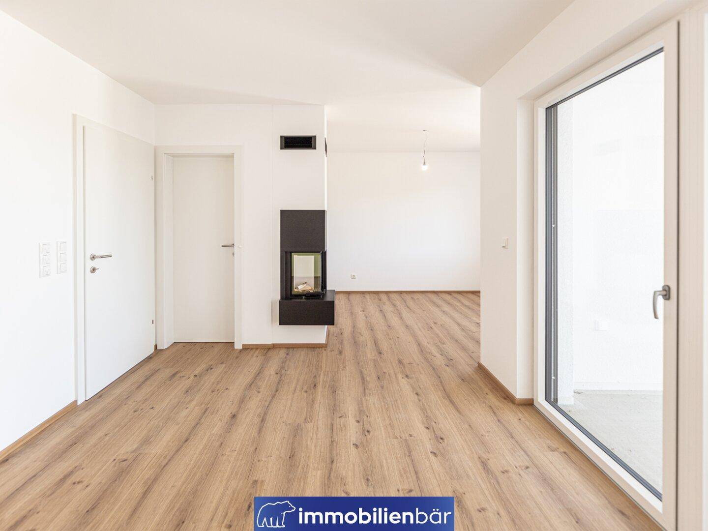 Geräumiger Wohnbereich mit Kamin und Zugang zur Terrasse durch große Fenster.