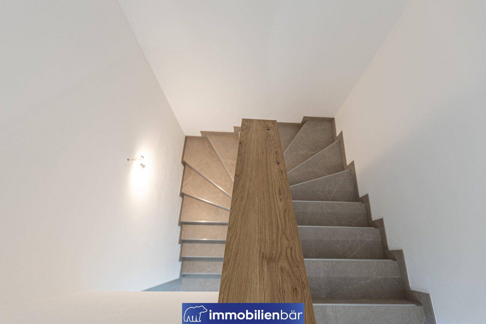Moderne Treppe mit Holzgeländer und gefliesten Stufen, die in die obere Etage führt.