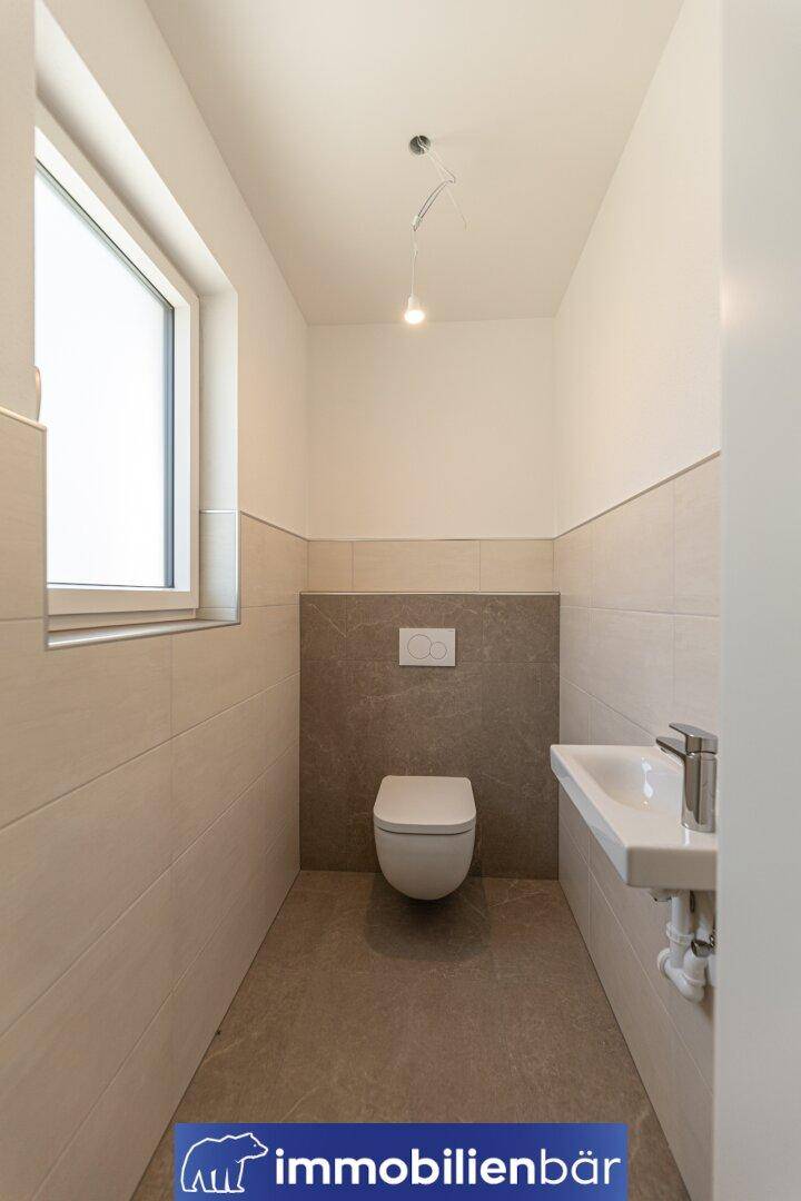 Helles Gäste-WC mit Fenster, wandhängender Toilette und kleinem Waschbecken.