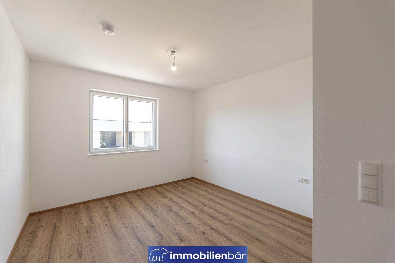Helles Schlafzimmer mit Laminatboden und großem Fenster, bereit zur individuellen Gestaltung.