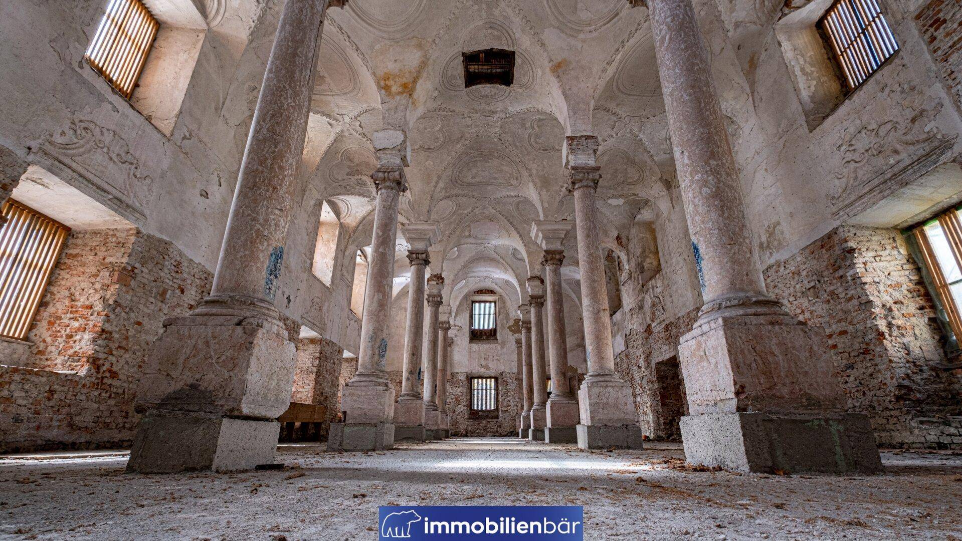 Großer, verfallener Saal mit zahlreichen Säulen und beeindruckenden Gewölbedecken, der auf eine reiche Geschichte hindeutet.