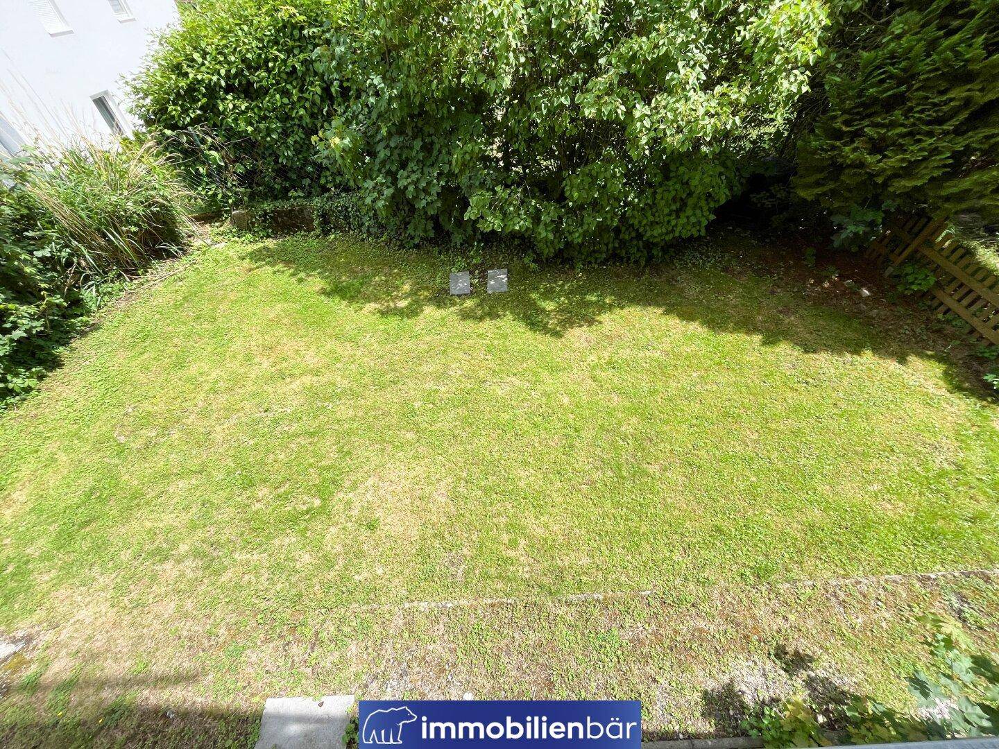 Gepflegte Rasenfläche im Gartenbereich, umgeben von dichtem Grün und Sträuchern.