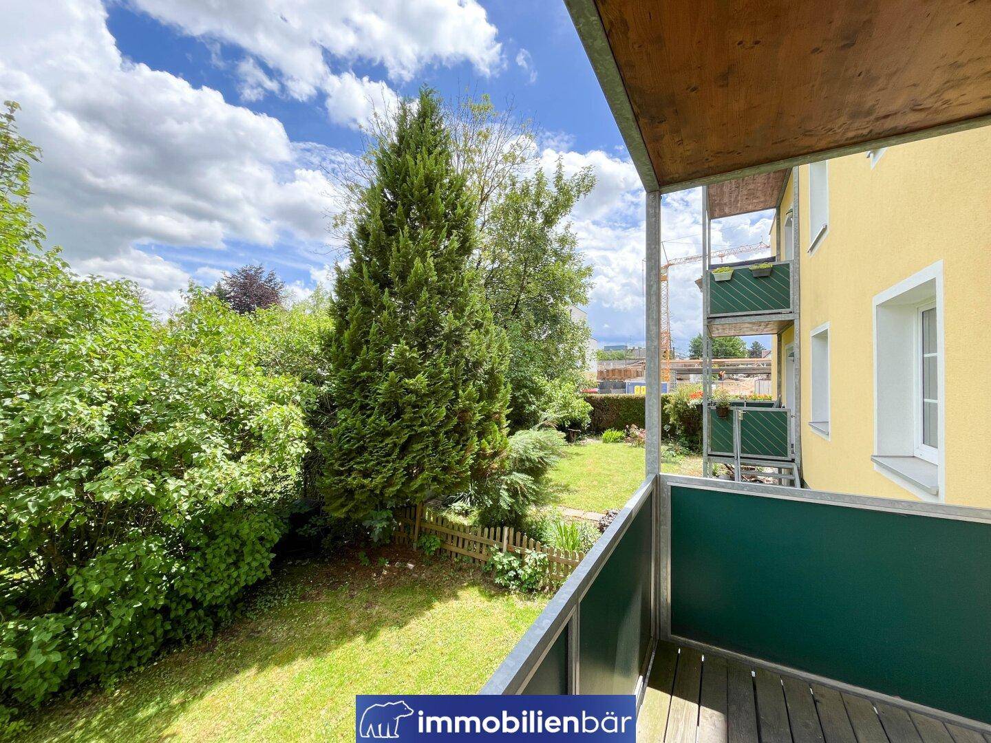 Balkon mit Holzboden und Blick auf den grünen Garten und umliegende Gebäude.