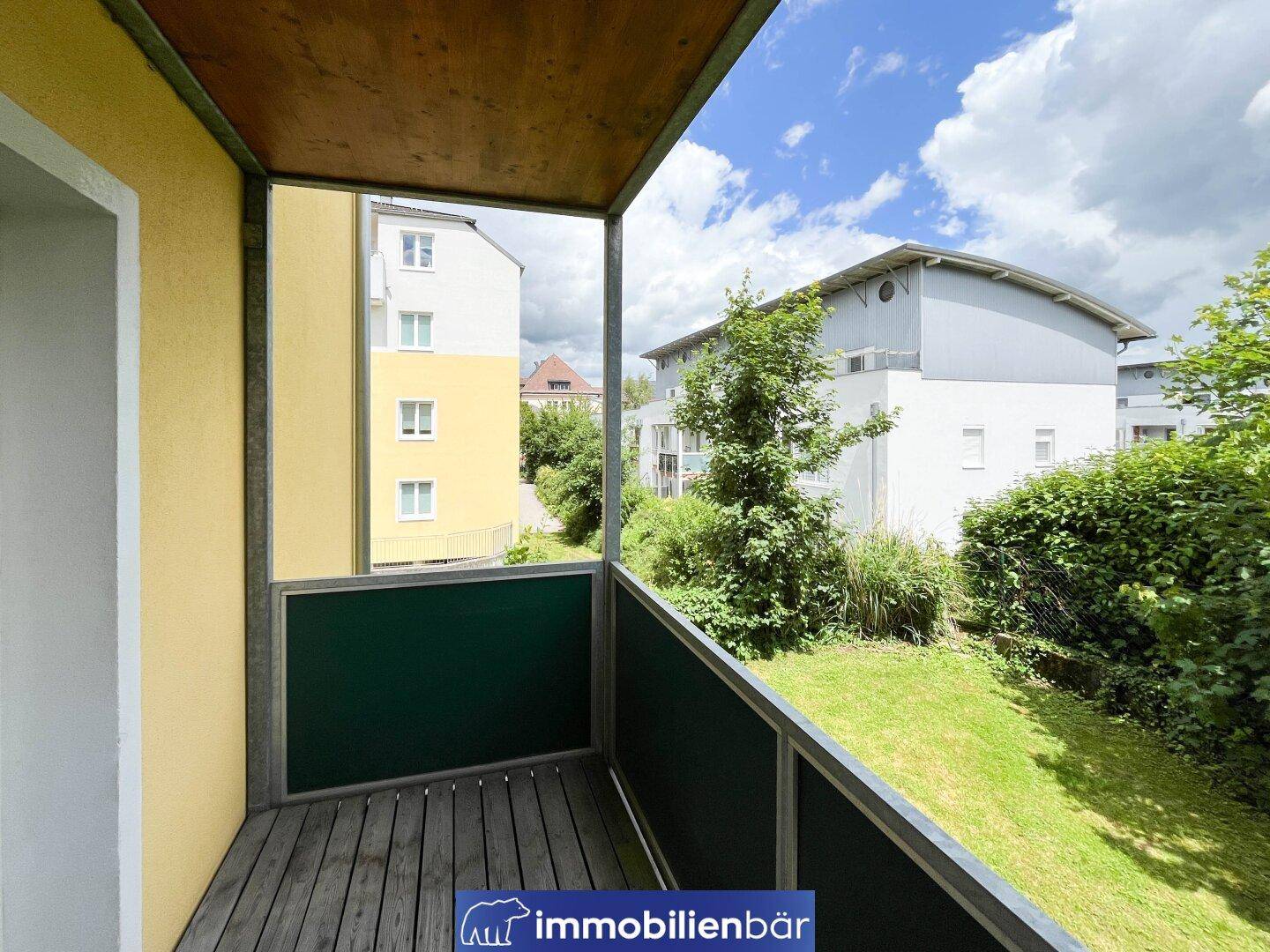 Balkon mit Holzboden und Blick auf die Nachbarschaft und grüne Umgebung.
