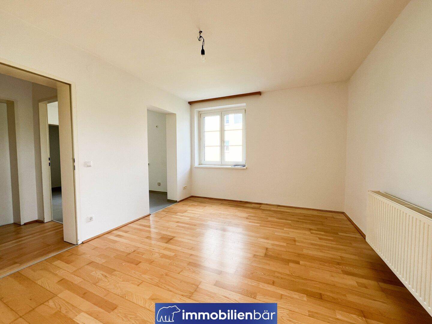 Geräumiges, helles Zimmer mit Parkettboden und weiß gestrichenen Wänden.