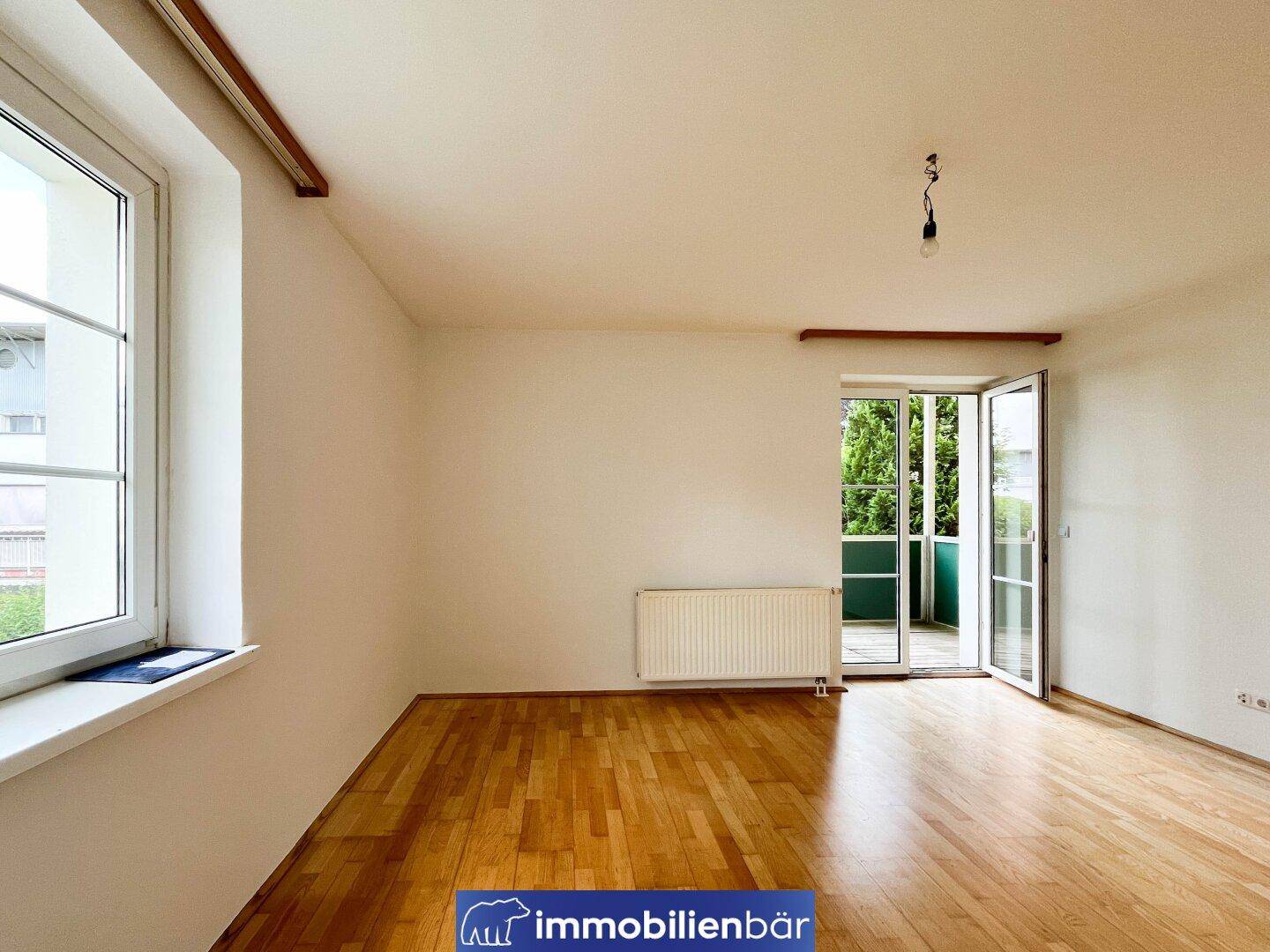 Helles, leeres Zimmer mit Parkettboden und Zugang zu einem Balkon.