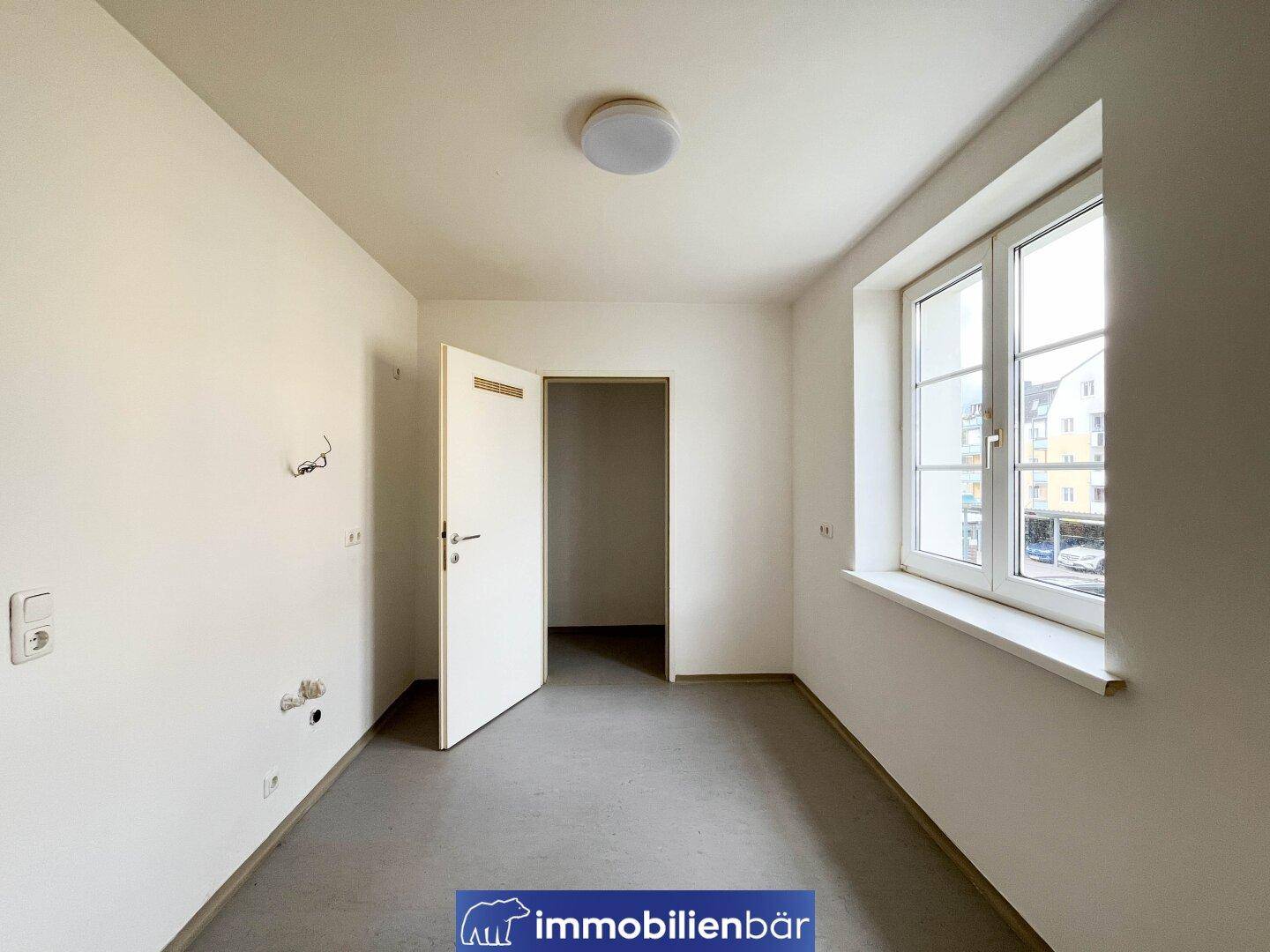 Kleiner Raum mit Fenster, grauen Fliesen und Anschlüssen an der Wand.